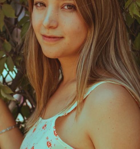 Customer-Focused - A young woman in a floral dress poses outdoors by a leafy fence, exuding a natural and serene vibe.