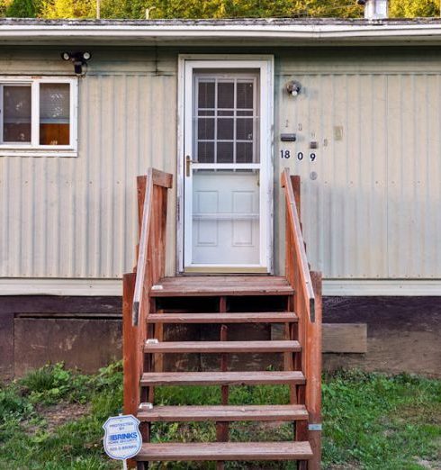 Entryway - Exterior view of a mobile home with wooden steps on a sunny day.