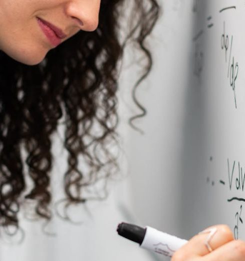 Workshops - Female engineer solving equations on whiteboard with focus and precision.