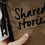 Storytelling - Hand holds a "Shared Stories" journal against a blurred outdoor backdrop, emphasizing creativity and personal storytelling.