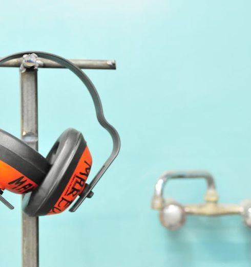 Safety - Close-up of earmuffs hanging on a metal stand in front of a teal wall.