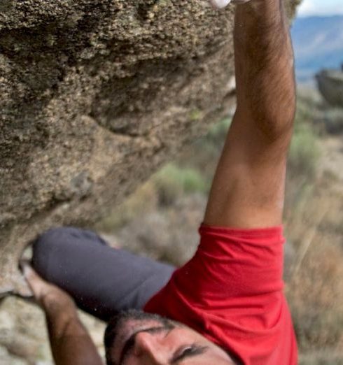 Challenges - Man in red shirt bouldering on a steep rock face, showcasing strength and determination.