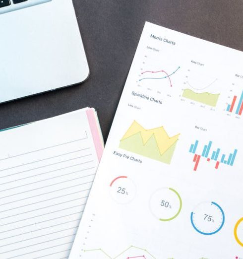 Data Visualization - Flatlay of business report with colorful charts, a notebook, and a laptop for data analysis on a desk.