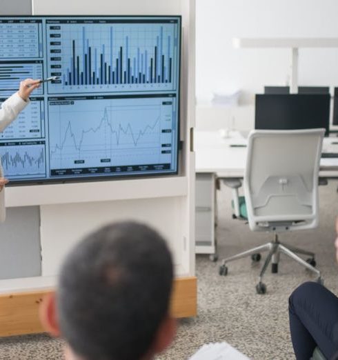 Data Reporting - A woman presents data on a screen to a group of colleagues in an open office environment.