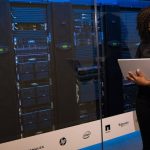 Data Management - A female engineer using a laptop while monitoring data servers in a modern server room.