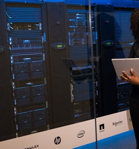 Data Management - A female engineer using a laptop while monitoring data servers in a modern server room.