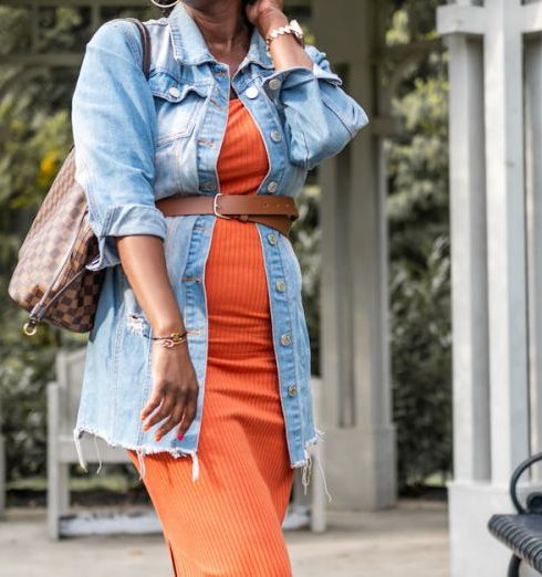 Benchmarking - Stylish woman in orange dress and denim jacket posing in a park gazebo during fall.