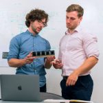 Product Development - Two men in an office discussing and reviewing a tech prototype.