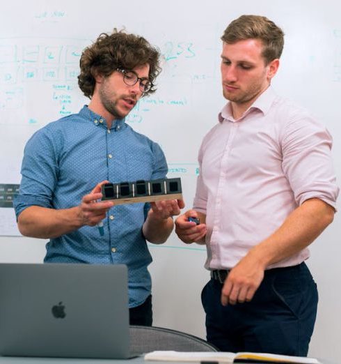 Product Development - Two men in an office discussing and reviewing a tech prototype.