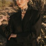 Trends - Stylish woman in a black blazer posing outdoors in Marrakesh with palm trees.