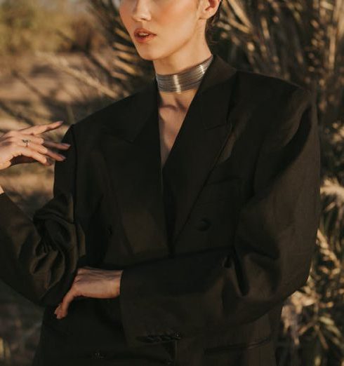 Trends - Stylish woman in a black blazer posing outdoors in Marrakesh with palm trees.