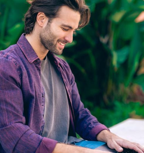 Going Global - Smiling Man in Purple Shirt Sitting and Working on Laptop