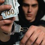 Trade Laws - Close-up of a handcuffed man holding cash and drugs, symbolizing crime and illegal trade.