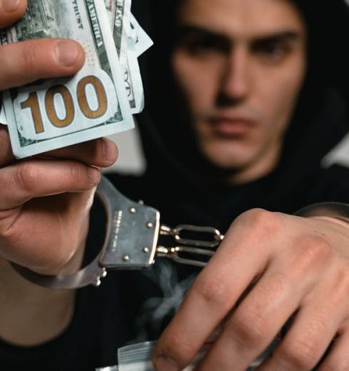 Trade Laws - Close-up of a handcuffed man holding cash and drugs, symbolizing crime and illegal trade.