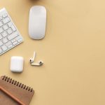 Technology - A minimalist workspace flat lay with keyboard, mouse, notebook, and succulent on a beige background.