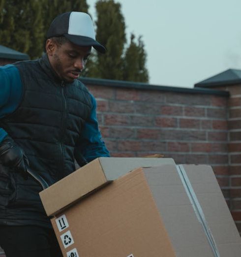 Distributors - Courier loading cardboard box into a van outdoors, showcasing logistics work.