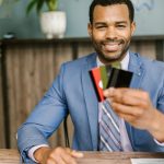 Payment Solutions - Smiling African American man in a suit holding credit cards at a business desk.