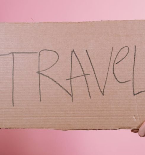 Cross-Border - Two hands holding a cardboard sign with 'TRAVEL' on a pink backdrop.