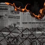 Political Risks - Dramatic image of hands holding a burning newspaper against a dark backdrop, with flames illuminating the scene.