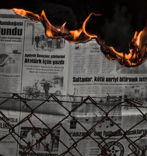 Political Risks - Dramatic image of hands holding a burning newspaper against a dark backdrop, with flames illuminating the scene.