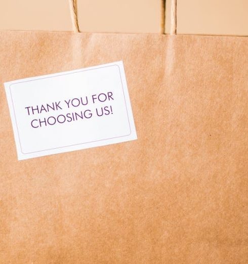 Brand Loyalty - A hand presents a brown paper shopping bag with a thank you note on a warm background.