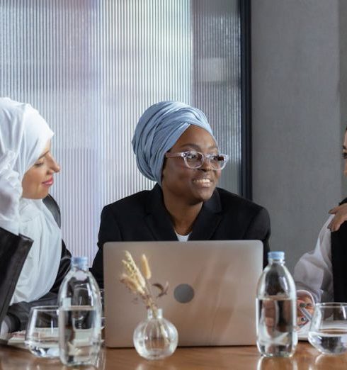 Cross-Cultural Collaboration - Three diverse women in hijabs discuss ideas around a table with a laptop, promoting inclusivity.