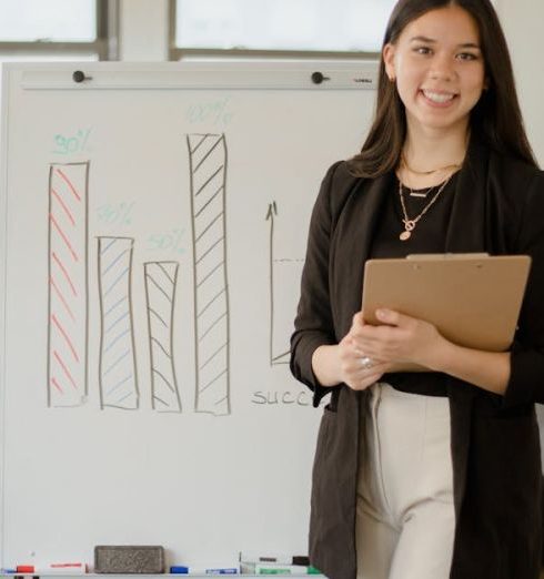 Success Metrics - Confident businesswoman presenting charts and data analysis on a whiteboard in a modern office setting.