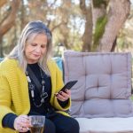 Outdoor Cushions - A Woman Holding a Cup of Tea while Using Her Cellphone