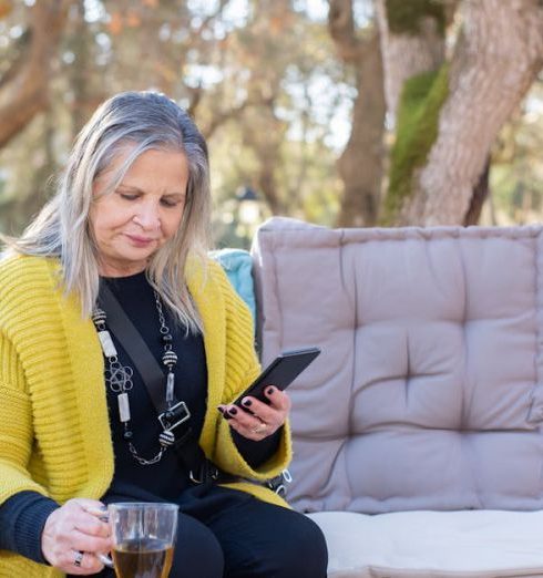 Outdoor Cushions - A Woman Holding a Cup of Tea while Using Her Cellphone