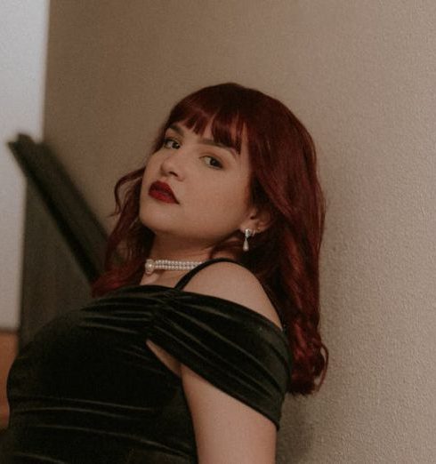 Furniture Arrangement - Sophisticated woman with red hair in a velvet dress posing on a staircase indoors.