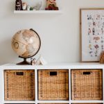 Furniture Arrangement - Comfortable bed with toys globe and paintings placed on wooden cabinet with wicker boxes and soft white rug with toy house on floor