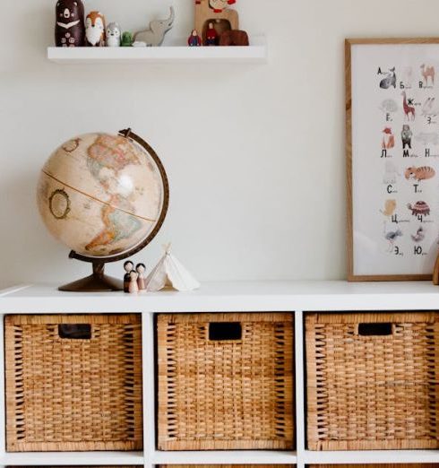 Furniture Arrangement - Comfortable bed with toys globe and paintings placed on wooden cabinet with wicker boxes and soft white rug with toy house on floor