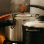 Pressure Cooker - A stove with two pots on it and steam coming out of them