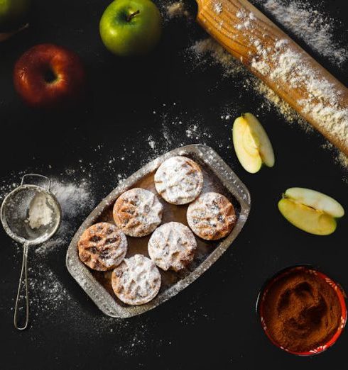 Bakeware - Flat lay of apple pie preparation with fresh apples, rolling pin, and pastry on dark surface.