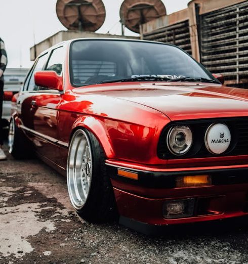 Customization - Classic red car displayed at a vibrant automotive meet with enthusiasts.