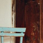 Minimalist Furniture - A rustic blue chair with a worn look sits against a vintage wooden wall.