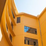 Architectural Features - Vibrant yellow building facade viewed from below, showcasing dynamic architecture and open sky.