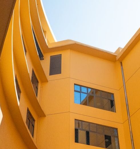 Architectural Features - Vibrant yellow building facade viewed from below, showcasing dynamic architecture and open sky.