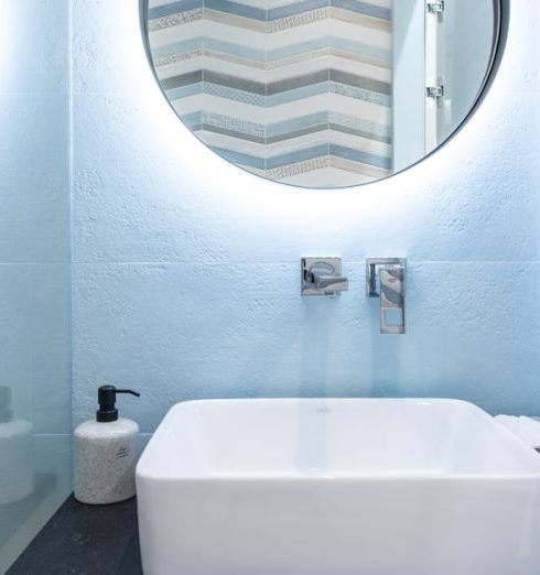 Floating Vanity - Interior of modern bright restroom with sink and tap on counter under round mirror on wall next to glass wall to shower