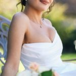 Natural Light - A beautiful bride in a white dress poses elegantly with a bouquet in a sunlit garden.