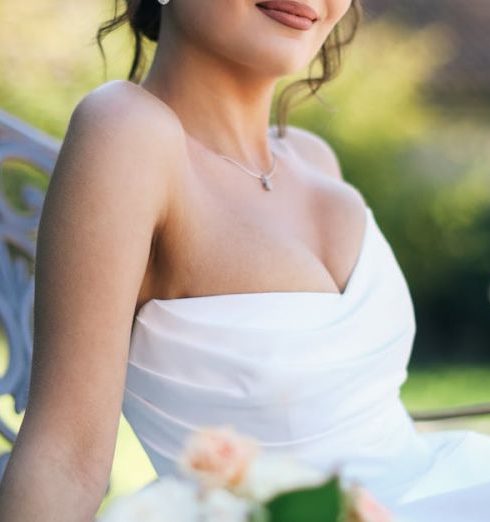 Natural Light - A beautiful bride in a white dress poses elegantly with a bouquet in a sunlit garden.