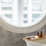 Freestanding Tub - Interior of contemporary bathroom with white bathtub and small table placed against concrete wall with round window in daylight