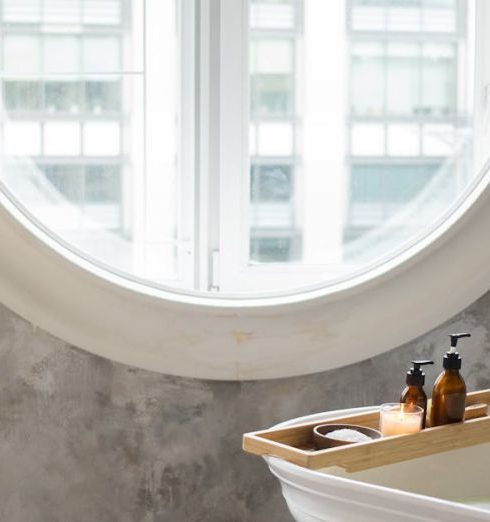 Freestanding Tub - Interior of contemporary bathroom with white bathtub and small table placed against concrete wall with round window in daylight