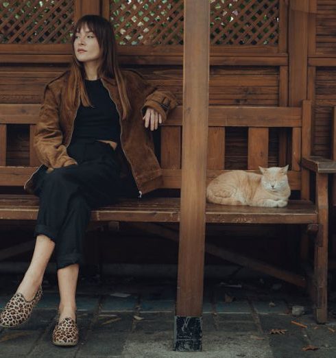 Pet Patio - A woman in casual attire enjoys a peaceful moment on a bench with a ginger cat in a cozy wooden outdoor setting.