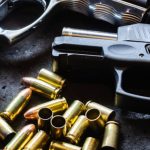 Self-Defense - Detailed shot of various handguns and bullets arranged on a textured dark surface, showcasing firearm elements.