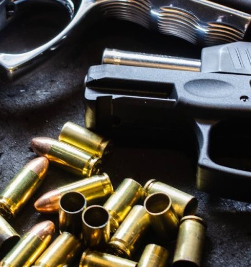 Self-Defense - Detailed shot of various handguns and bullets arranged on a textured dark surface, showcasing firearm elements.