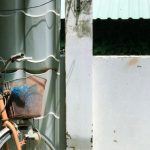 Storage Wall - A vintage bicycle with a basket stands against a textured urban wall under sunlight.