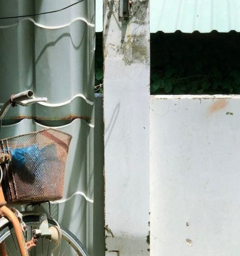 Storage Wall - A vintage bicycle with a basket stands against a textured urban wall under sunlight.