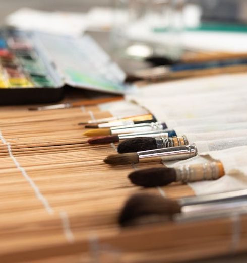 Craft Supplies - A collection of paint brushes and watercolor set on a bamboo mat, ready for artistic creation.