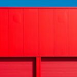 Outdoor Storage - Bright red garage doors of an industrial building against a clear blue sky, showcasing minimalism.